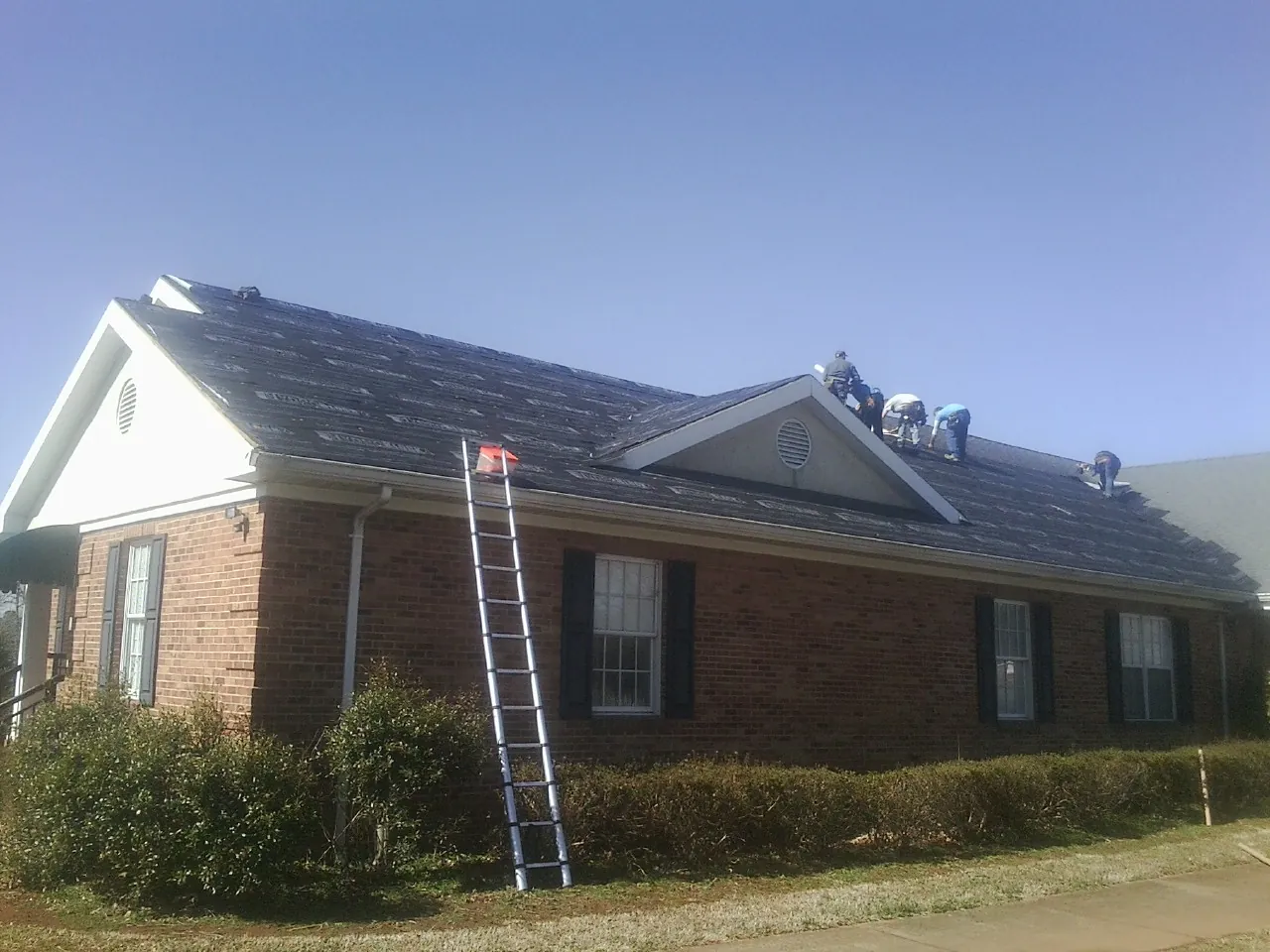 Crew tearing shingles off a brick ranch roof with a ladder set — Metal Roof Repair work by our crew in Shrub Oak