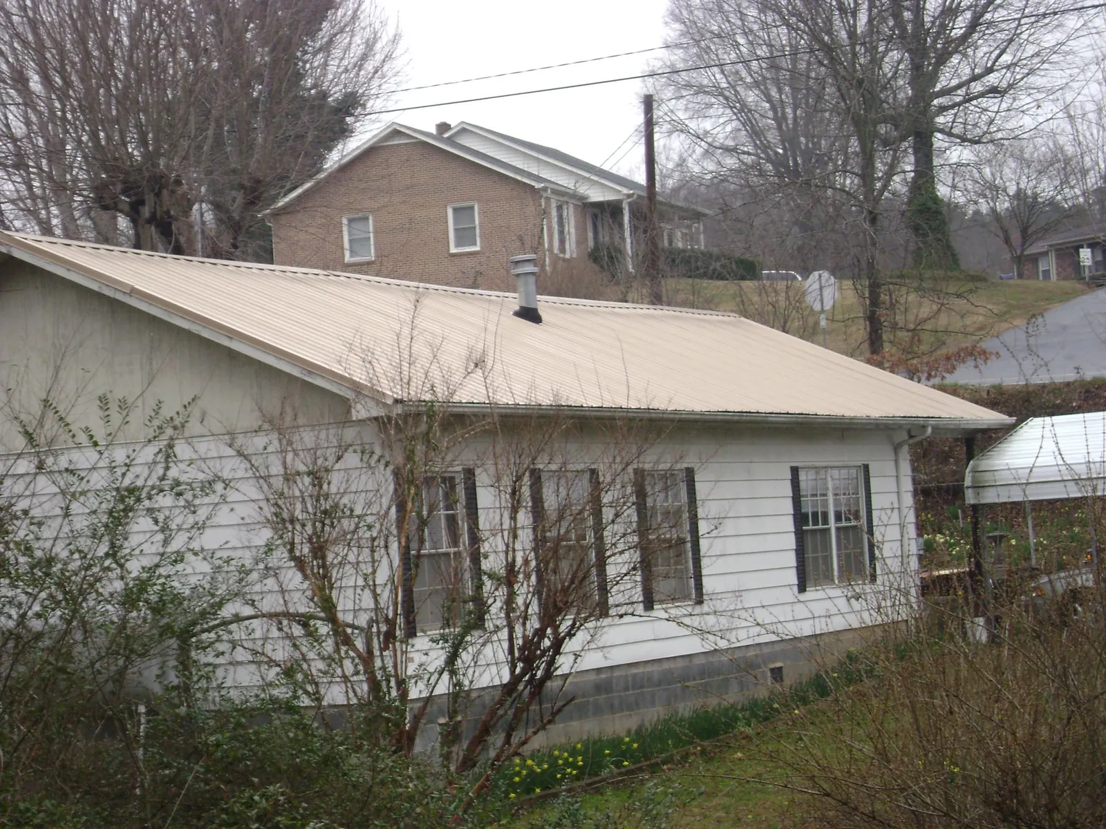 Tan metal roof on a white sided house set into a hillside — Commercial Roofing by Roofing Brothers in Shrub Oak